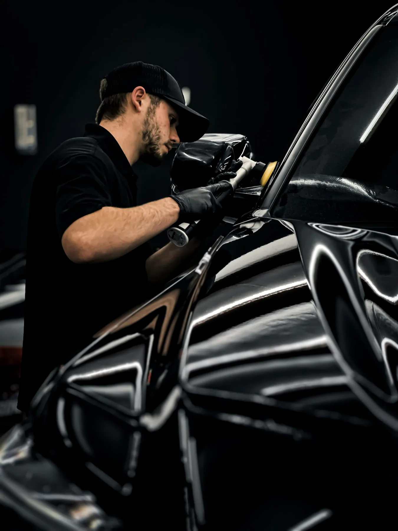 A detailer uses a polishing tool on the reflective side of a black car.